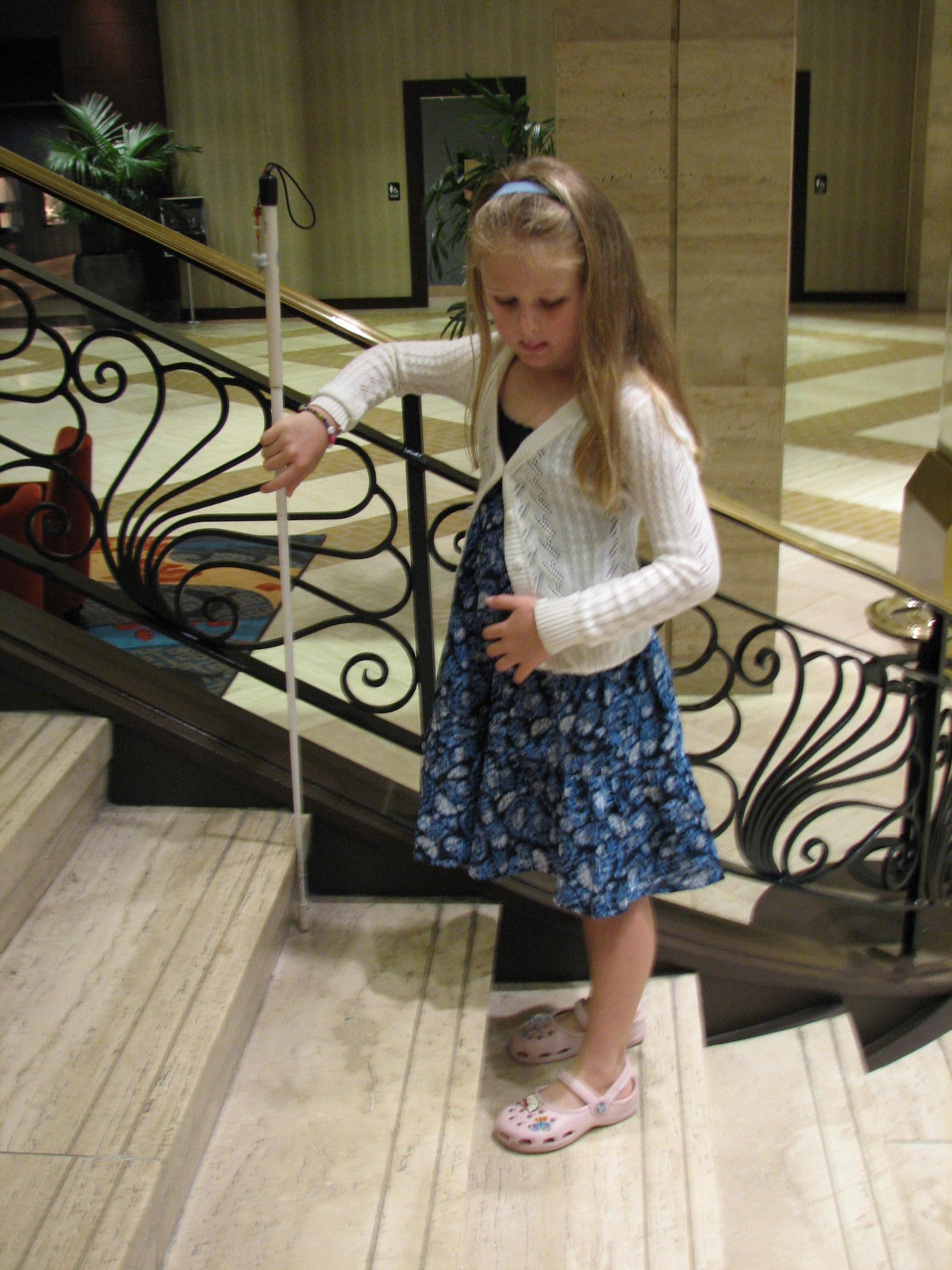 Child uses long white cane to go up stairs